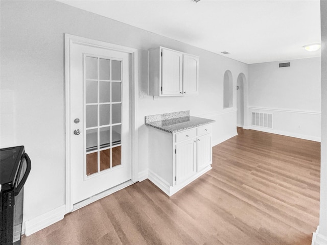 kitchen featuring light wood finished floors, visible vents, baseboards, stone counters, and white cabinetry