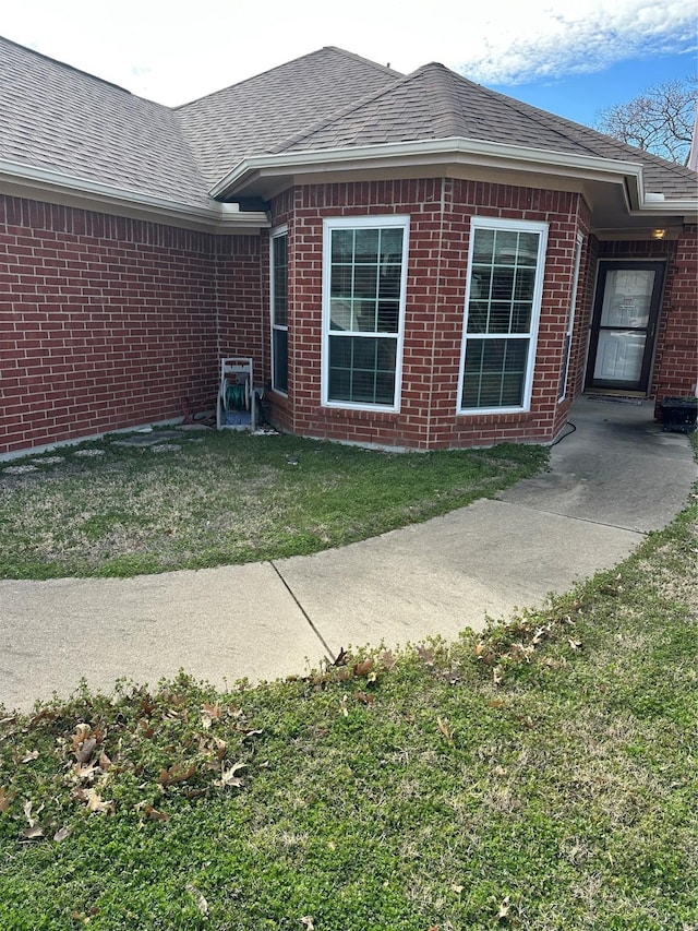 view of side of home with a shingled roof, brick siding, and a lawn