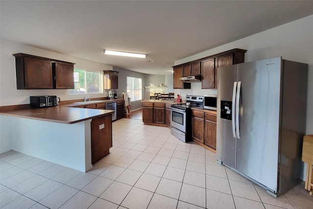 kitchen featuring light tile patterned flooring, dark brown cabinetry, under cabinet range hood, stainless steel appliances, and a peninsula