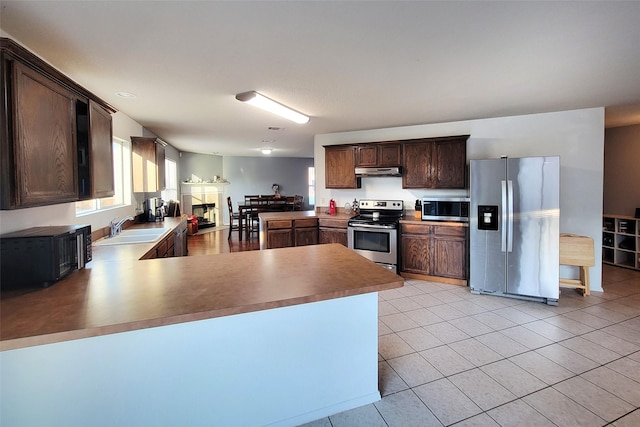 kitchen with light tile patterned flooring, under cabinet range hood, stainless steel appliances, a peninsula, and a sink