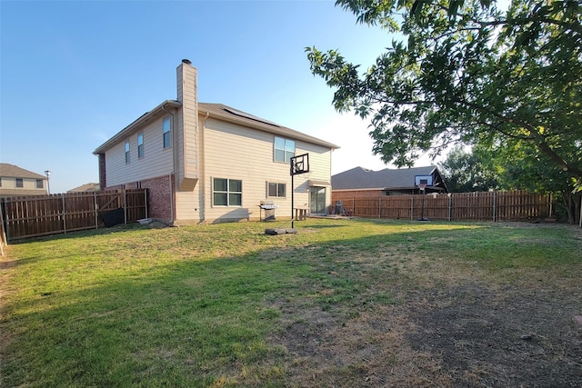 back of house featuring a fenced backyard, a lawn, and a chimney