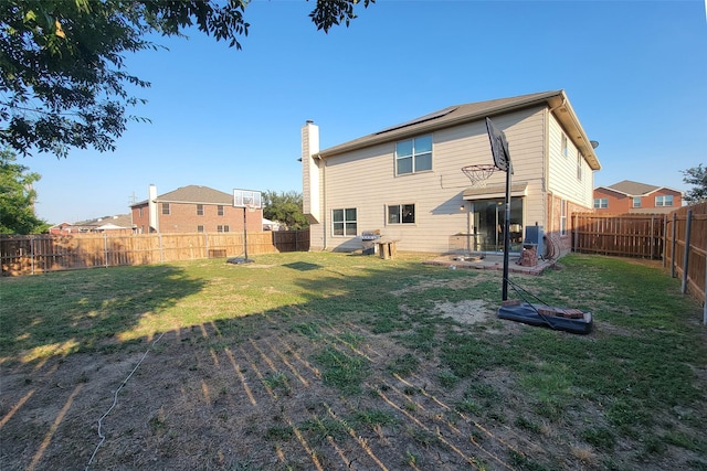 rear view of property featuring a fenced backyard, a lawn, a chimney, and solar panels