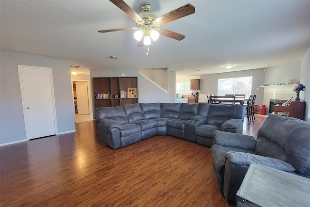 living area featuring wood finished floors, visible vents, baseboards, a ceiling fan, and a tiled fireplace