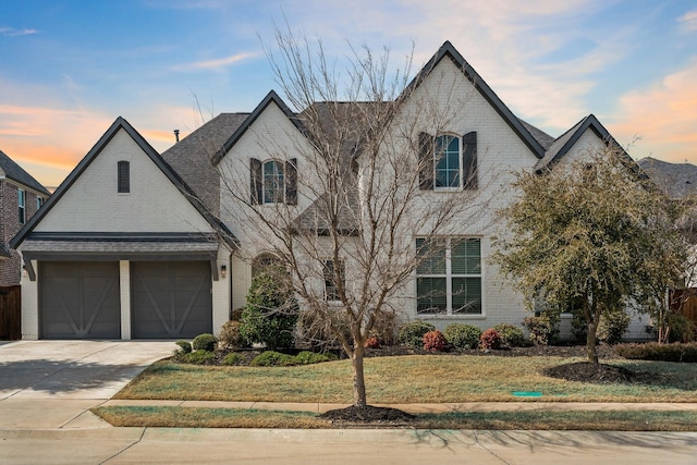 french provincial home featuring an attached garage, driveway, brick siding, and a front yard