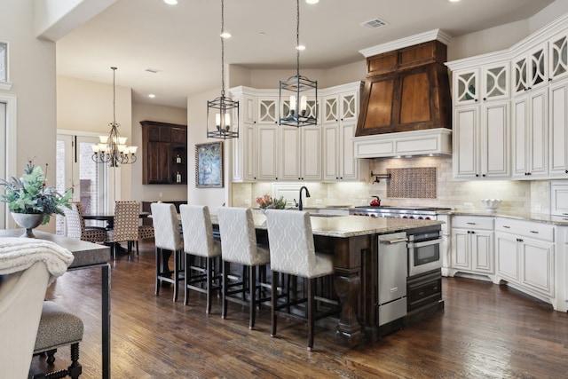 kitchen with a kitchen island with sink, a breakfast bar, light stone countertops, glass insert cabinets, and pendant lighting