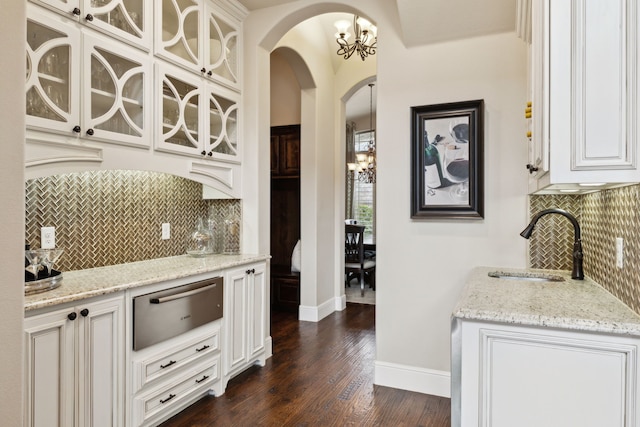 kitchen featuring arched walkways, white cabinets, light stone countertops, a notable chandelier, and a warming drawer