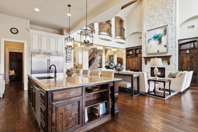 kitchen featuring a center island with sink, visible vents, white cabinets, decorative light fixtures, and a sink