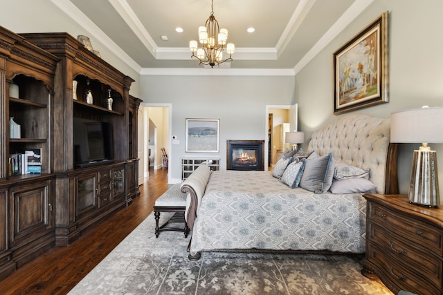 bedroom with crown molding, a glass covered fireplace, a raised ceiling, and dark wood finished floors