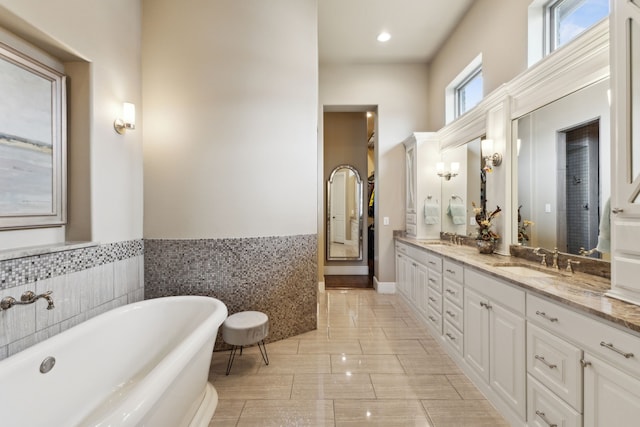 full bath with double vanity, a soaking tub, tile walls, and a sink