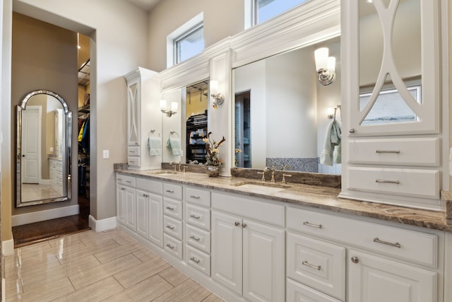 full bath with double vanity, a walk in closet, and a sink