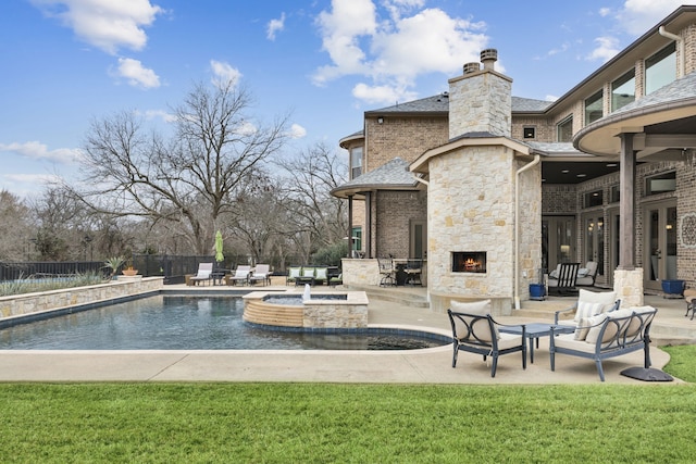 view of swimming pool featuring an outdoor stone fireplace, fence, a pool with connected hot tub, a lawn, and a patio area