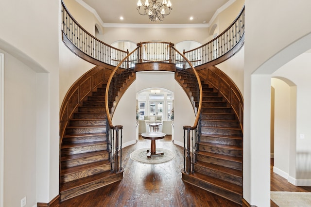 stairway with crown molding, a towering ceiling, an inviting chandelier, wood finished floors, and baseboards