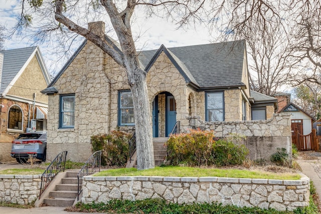 tudor home featuring a shingled roof and stone siding