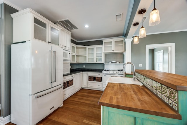 kitchen featuring white appliances, white cabinets, butcher block counters, glass insert cabinets, and decorative light fixtures