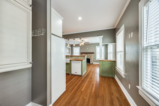 kitchen with a stone fireplace, white dishwasher, wood finished floors, a ceiling fan, and crown molding