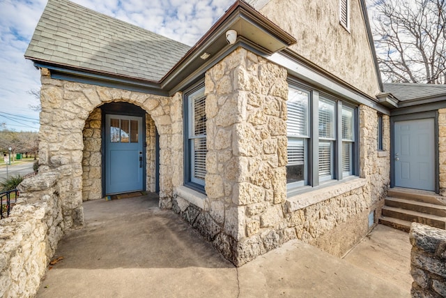 entrance to property with stone siding and roof with shingles