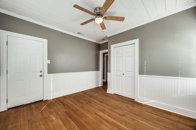 unfurnished room with a wainscoted wall, wood finished floors, visible vents, and crown molding