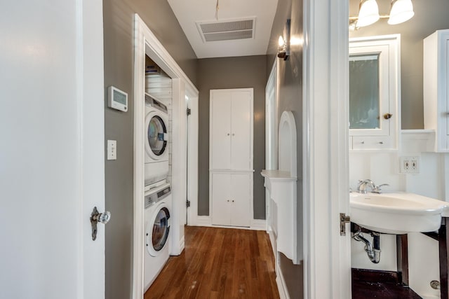 laundry room featuring dark wood-style floors, laundry area, visible vents, and stacked washing maching and dryer