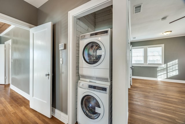 laundry area featuring visible vents, stacked washing maching and dryer, wood finished floors, laundry area, and baseboards