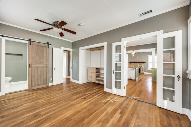 unfurnished bedroom featuring french doors, a barn door, ornamental molding, wood finished floors, and baseboards