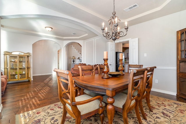 dining room with arched walkways, visible vents, a raised ceiling, and dark wood finished floors