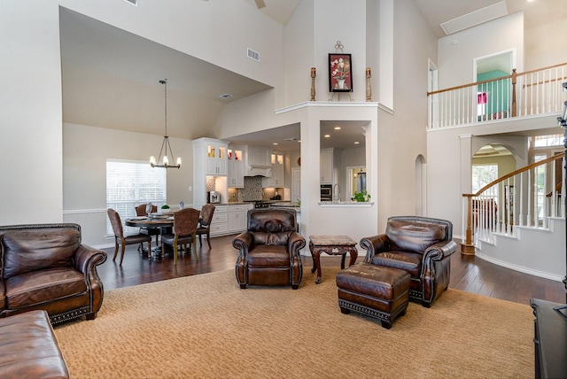 living room with a notable chandelier, visible vents, wood finished floors, high vaulted ceiling, and stairs