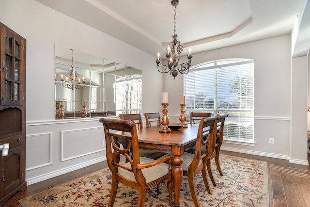 dining room with dark wood-type flooring, a tray ceiling, a chandelier, and a decorative wall