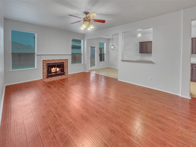 unfurnished living room with a ceiling fan, a fireplace, light wood-style flooring, and baseboards