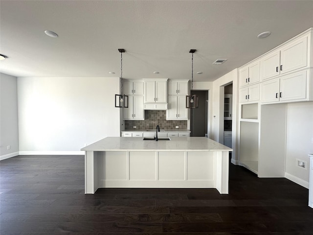 kitchen featuring a sink, white cabinets, tasteful backsplash, an island with sink, and decorative light fixtures