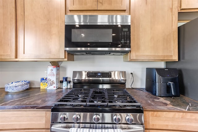 kitchen with stainless steel appliances, dark countertops, and light brown cabinetry