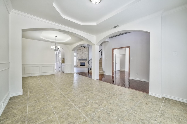 empty room featuring visible vents, arched walkways, tile patterned flooring, a tray ceiling, and a decorative wall