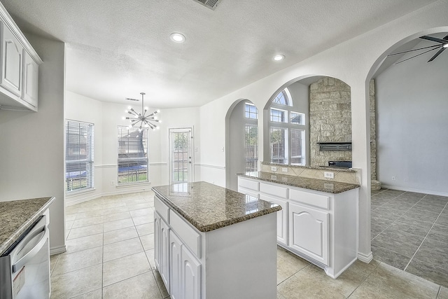 kitchen featuring decorative light fixtures, stainless steel dishwasher, white cabinetry, a kitchen island, and dark stone counters