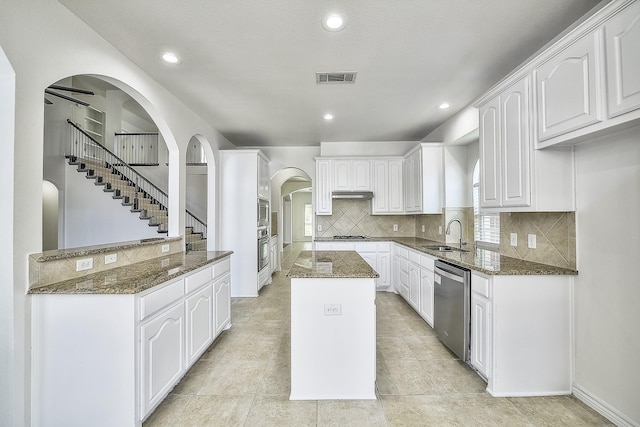 kitchen with a center island, appliances with stainless steel finishes, white cabinetry, a sink, and dark stone counters