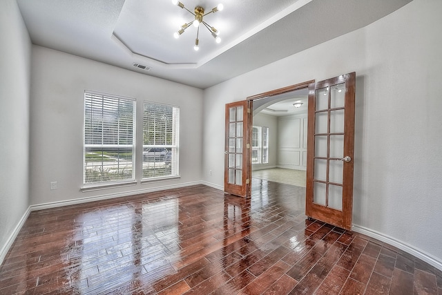 unfurnished room featuring arched walkways, dark wood-type flooring, visible vents, french doors, and a tray ceiling