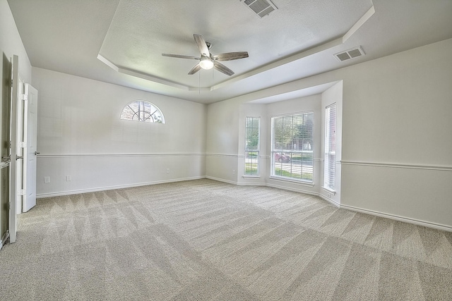 empty room featuring baseboards, a tray ceiling, visible vents, and light colored carpet