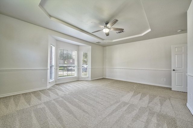 empty room featuring carpet floors, a tray ceiling, visible vents, and baseboards