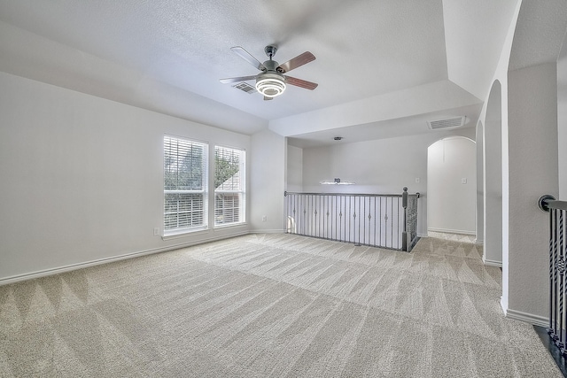 unfurnished room featuring light carpet, visible vents, arched walkways, and baseboards