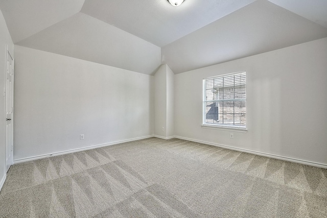 spare room featuring carpet, vaulted ceiling, and baseboards