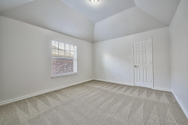 carpeted spare room with vaulted ceiling and baseboards