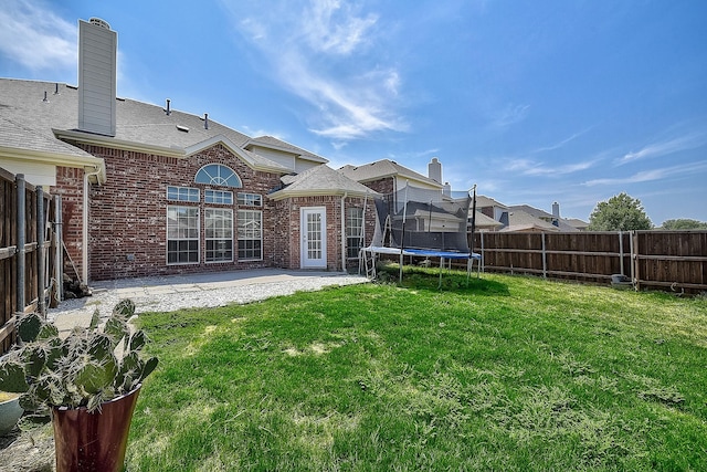 back of property with brick siding, a trampoline, a patio area, and a fenced backyard