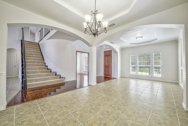 tiled foyer featuring visible vents, a tray ceiling, arched walkways, and a notable chandelier