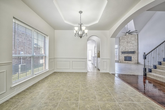 interior space with a tray ceiling, light tile patterned floors, ceiling fan with notable chandelier, a decorative wall, and stairs