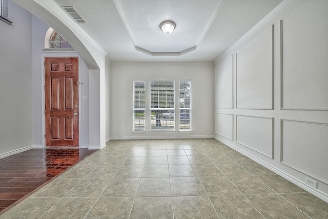 tiled entrance foyer with arched walkways, a tray ceiling, visible vents, a decorative wall, and a textured ceiling