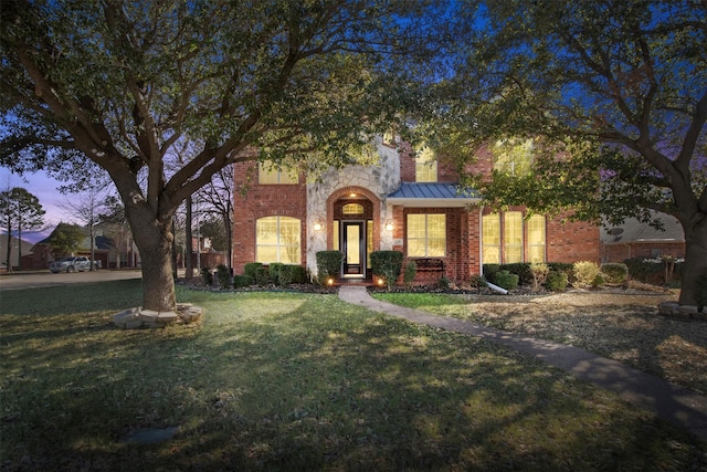 traditional-style home with a standing seam roof, metal roof, a lawn, and brick siding