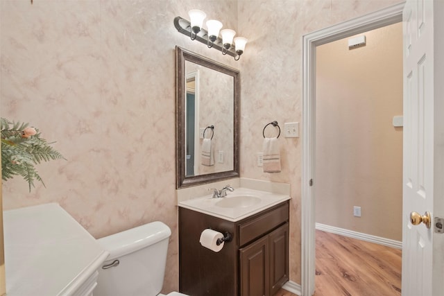 half bathroom featuring toilet, vanity, wood finished floors, baseboards, and wallpapered walls