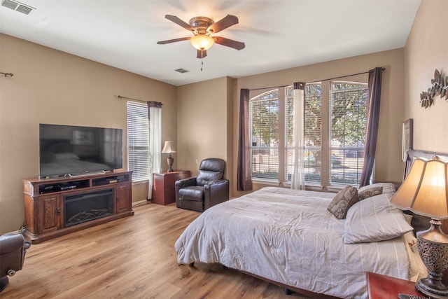 bedroom featuring a ceiling fan, visible vents, a fireplace, and light wood-style flooring