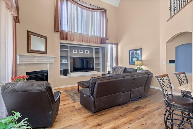 living area with arched walkways, light wood-style flooring, a high ceiling, baseboards, and a tiled fireplace