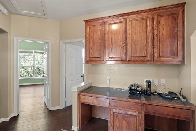 kitchen featuring dark wood-type flooring, brown cabinetry, dark countertops, and baseboards