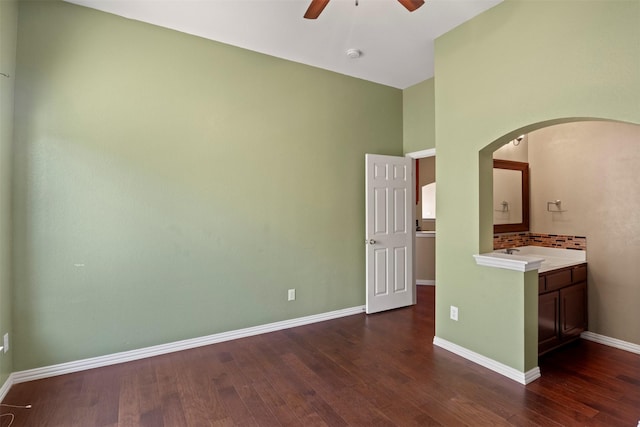 empty room with dark wood-type flooring, arched walkways, ceiling fan, and baseboards