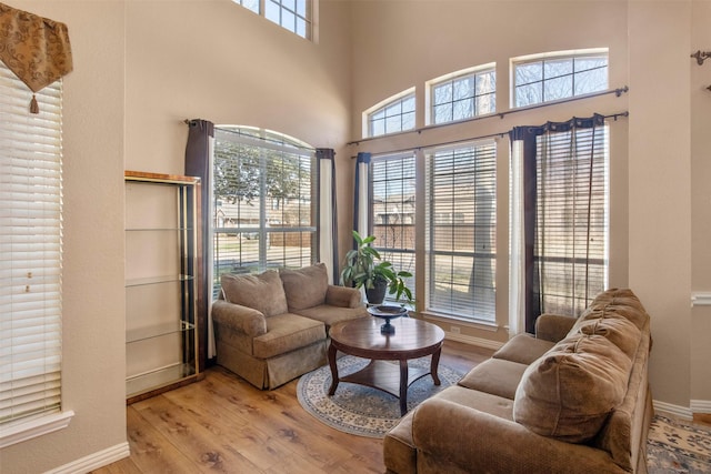 living room with a high ceiling, plenty of natural light, wood finished floors, and baseboards